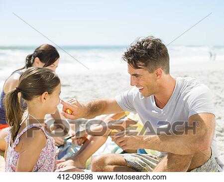 Stock Photo - Father rubbing sunscreen on daughter's nose at beach. Fotosearch