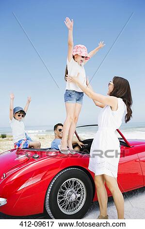 Stock Photo - Girl jumping into mother's arms from convertible at beach. Fotosearch