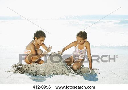 Stock Image - Girls building sandcastle on beach. Fotosearch