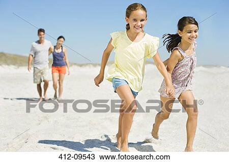 Stock Image - Girls holding hands and running on beach. Fotosearch
