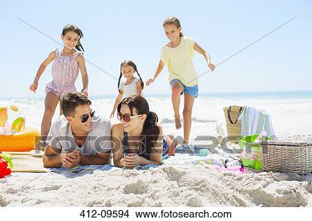 Picture - Girls running toward parents laying on beach. Fotosearch
