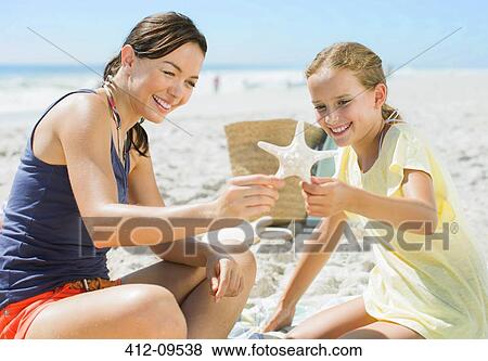 Stock Photo - Mother and daughter examining starfish on beach. Fotosearch