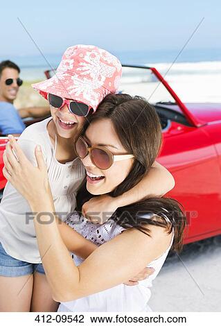 Stock Image - Mother and daughter hugging by convertible. Fotosearch