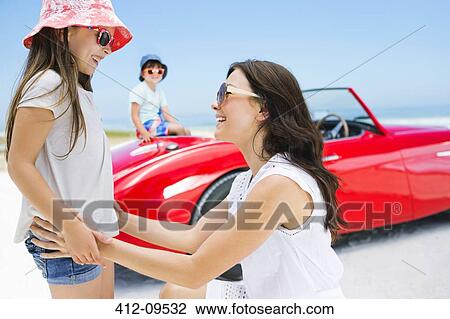 Mother and daughter smiling on beach near convertible View Large Photo Image Stock Image - Mother and daughter smiling on beach near convertible. Fotosearch