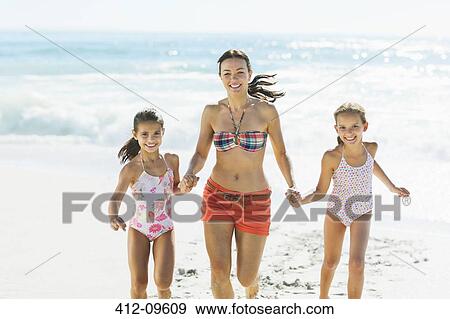 Stock Photo - Mother and daughters holding hands and running on beach. Fotosearch