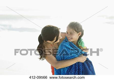 Stock Photograph - Mother wrapping daughter in towel on beach. Fotosearch