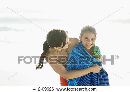 Stock Photograph - Mother wrapping daughter in towel on beach. Fotosearch