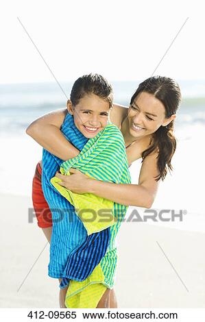 Stock Photography - Mother wrapping daughter in towel on beach. Fotosearch