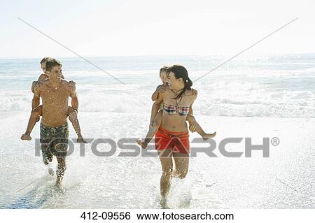 Parents carrying daughters piggyback in surf at beach View Large Photo Image Stock Photograph - Parents carrying daughters piggyback in surf at beach. Fotosearch