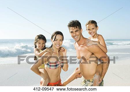 Stock Photo - Parents carrying daughters piggyback on beach. Fotosearch