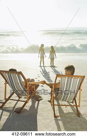Stock Image - Parents watching daughters on beach at sunset. Fotosearch