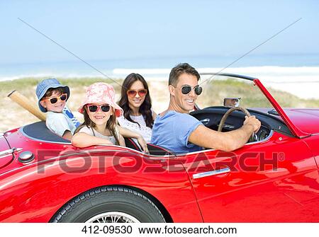 Stock Image - Portrait of smiling family in convertible at beach. Fotosearch