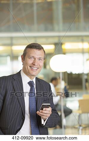 Stock Image - Businessman using cell phone in office. Fotosearch