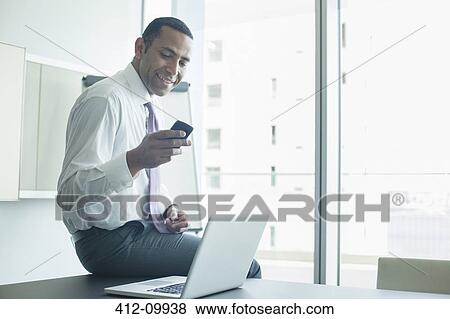 Stock Photo - Businessman using cell phone in office. Fotosearch
