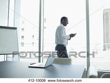 Stock Photo - Businessman using cell phone in office. Fotosearch
