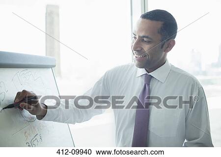 Stock Image - Businessman writing on whiteboard in office. Fotosearch