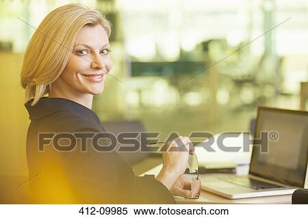 Stock Photography - Businesswoman smiling at desk in office. Fotosearch