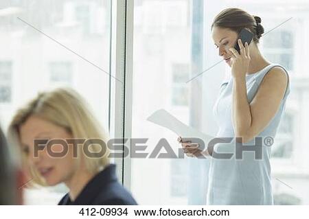 Picture - Businesswoman talking on cell phone in office. Fotosearch
