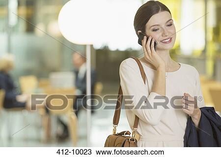 Stock Image - Businesswoman talking on cell phone in office. Fotosearch