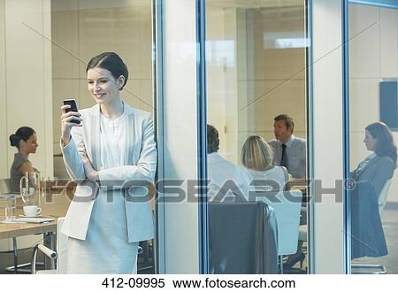 Stock Photography - Businesswoman using cell phone in meeting. Fotosearch
