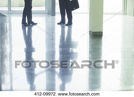 Stock Image - Reflection of businessmen shaking hands in office lobby. Fotosearch