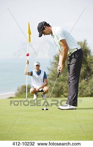 Stock Image - Caddy watching man putt. Fotosearch