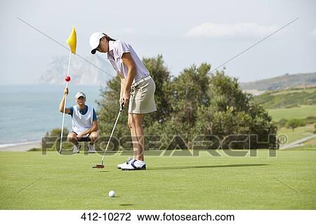 Caddy watching woman putt on golf course View Large Photo Image Stock Image - Caddy watching woman putt on golf course. Fotosearch