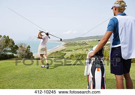 Caddy watching woman tee off on golf course overlooking ocean View Large Photo Image Stock Photography - Caddy watching woman tee off on golf course overlooking ocean. Fotosearch