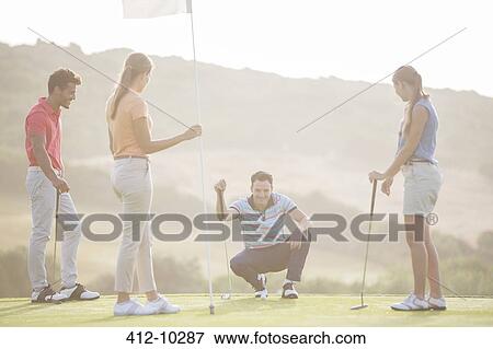 Friends watching man prepare to putt on golf course View Large Photo Image Stock Photo - Friends watching man prepare to putt on golf course. Fotosearch