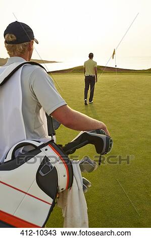 Stock Image - Golfer and caddy nearing golf flag. Fotosearch