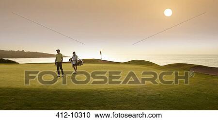 Stock Image - Golfer and caddy walking on golf course. Fotosearch