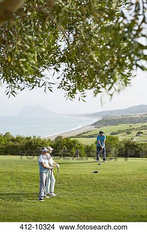 Picture - Older friends playing golf on course. Fotosearch