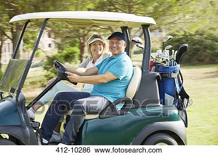 Stock Photograph - Senior couple driving golf cart on course. Fotosearch