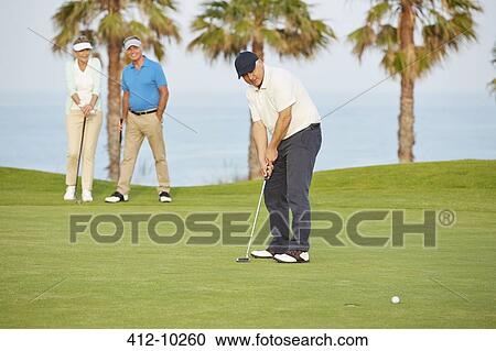 Stock Image - Senior friends playing golf on course. Fotosearch