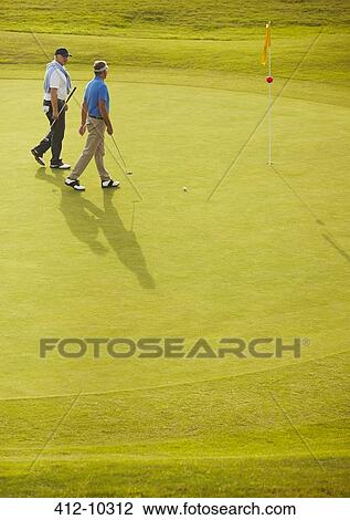 Stock Image - Senior men walking on golf course. Fotosearch