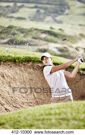 Stock Image - Woman swinging from sand trap on golf course. Fotosearch