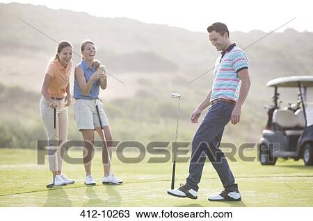 Stock Image - Women watching man balance golf club on foot. Fotosearch