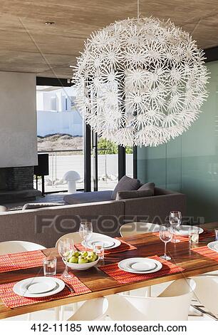 Stock Photography - Chandelier over set dining table in modern dining room. Fotosearch