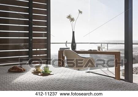 Stock Photo - Coffee and pastries on bed in modern bedroom overlooking ocean. Fotosearch
