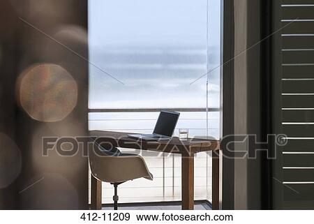 Stock Photo - Laptop on desk in modern home office overlooking ocean. Fotosearch