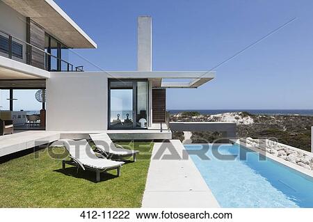 Stock Image - Lounge chairs and lap pool outside modern house. Fotosearch
