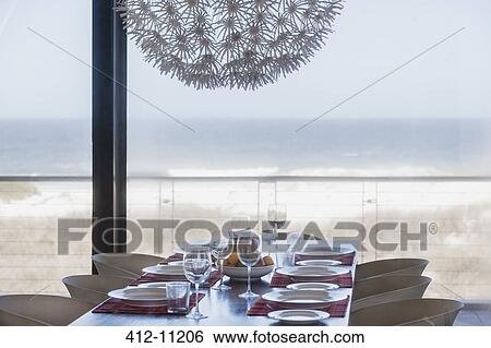 Stock Photograph - Set table in modern dining room overlooking ocean. Fotosearch