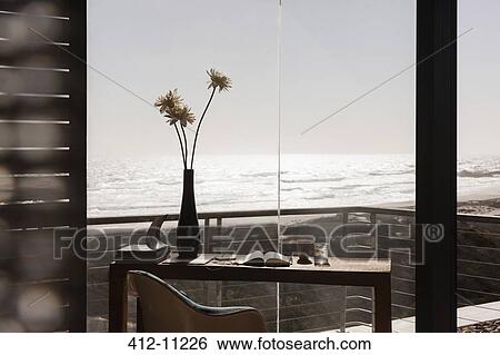 Stock Photograph - Vase of flowers on desk in modern home office overlooking ocean. Fotosearch