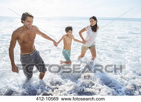 Family playing in waves at beach View Large Photo Image Stock Photo - Family playing in waves at beach. Fotosearch