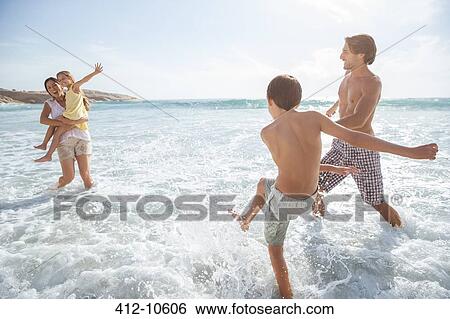 Family playing together in waves on beach View Large Photo Image Stock Photograph - Family playing together in waves on beach. Fotosearch