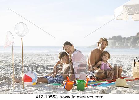 Stock Image - Family relaxing together on beach. Fotosearch