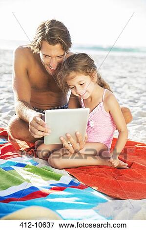 Stock Photo - Father and daughter using digital tablet on beach. Fotosearch