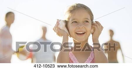 Girl listening to conch shells on beach View Large Photo Image Stock Image - Girl listening to conch shells on beach. Fotosearch