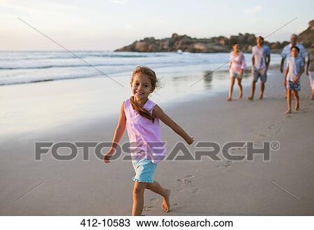 Girl walking on beach with family in background View Large Photo Image Stock Image - Girl walking on beach with family in background. Fotosearch