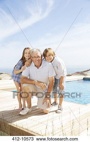 Stock Image - Grandfather and grandchildren smiling at poolside. Fotosearch